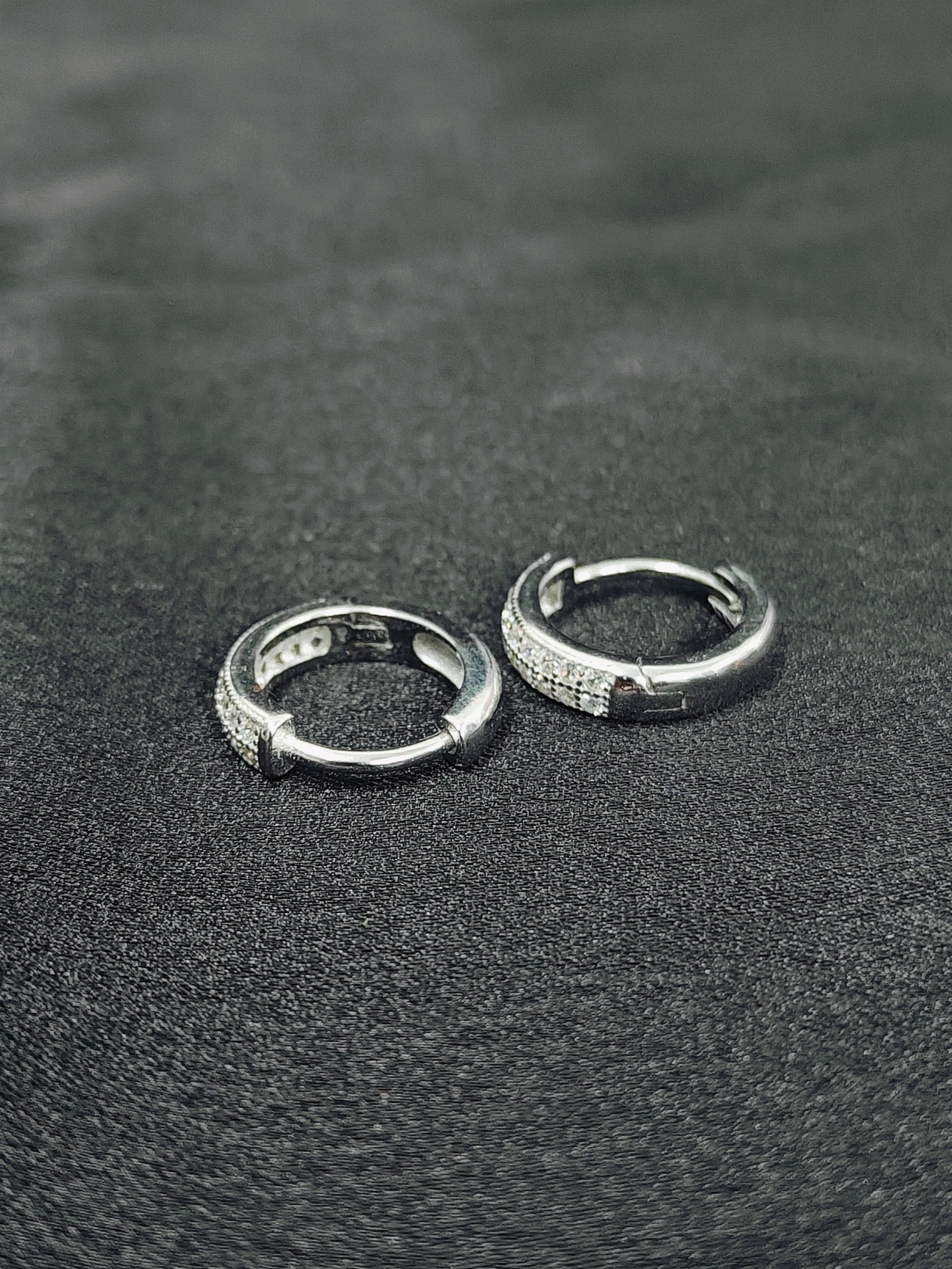 Two silver hoop earrings on a textured black surface
